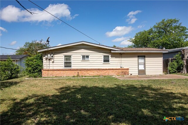back of house featuring a lawn, fence, and brick siding