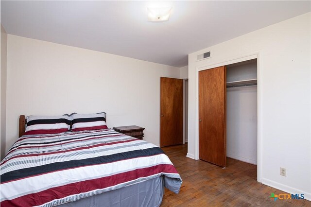 bedroom with baseboards, visible vents, wood finished floors, and a closet
