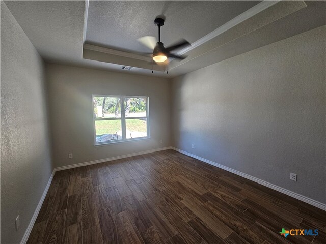 spare room with baseboards, visible vents, dark wood finished floors, a tray ceiling, and a textured ceiling