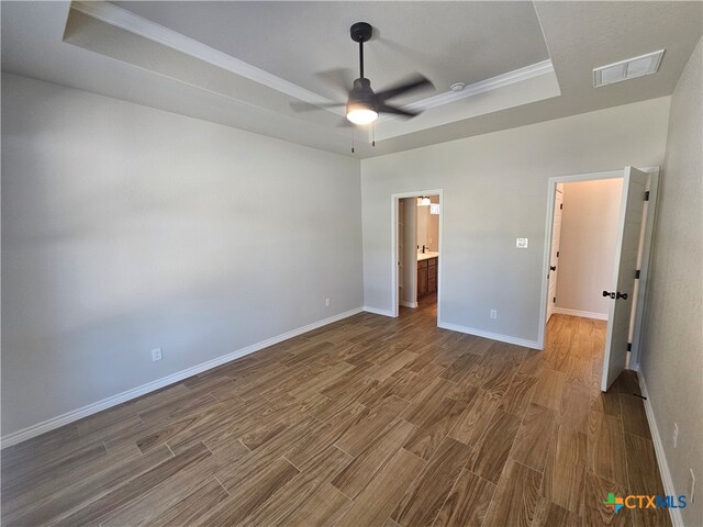 unfurnished bedroom featuring visible vents, dark wood finished floors, baseboards, ensuite bath, and a tray ceiling