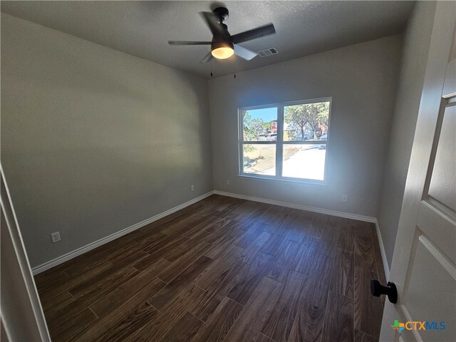 empty room with dark wood-type flooring, visible vents, baseboards, and a ceiling fan