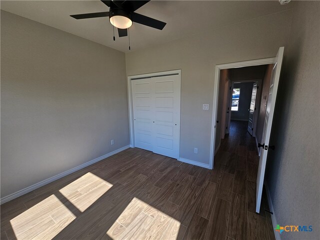 unfurnished bedroom with ceiling fan, a closet, baseboards, and dark wood-type flooring