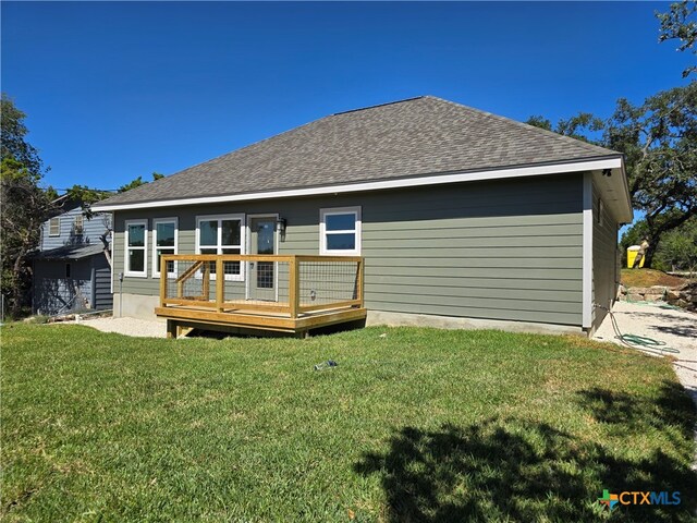 rear view of property featuring a deck, a lawn, and roof with shingles