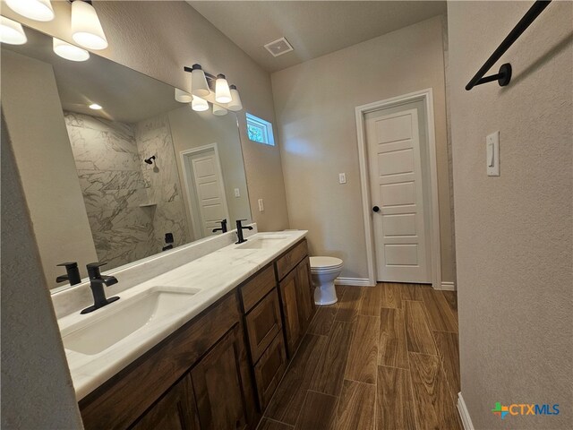 full bath with wood finish floors, visible vents, a sink, and a tile shower