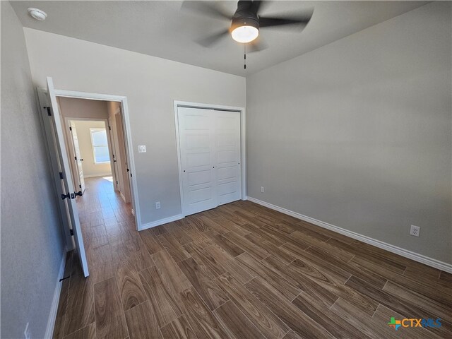 unfurnished bedroom with dark wood-style floors, a closet, baseboards, and a ceiling fan