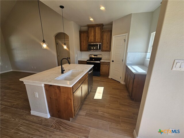 kitchen with a sink, light countertops, appliances with stainless steel finishes, backsplash, and decorative light fixtures