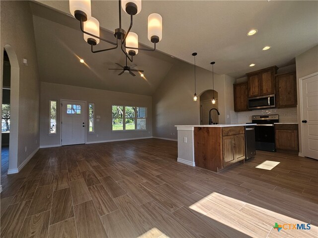 kitchen featuring arched walkways, appliances with stainless steel finishes, open floor plan, light countertops, and a sink