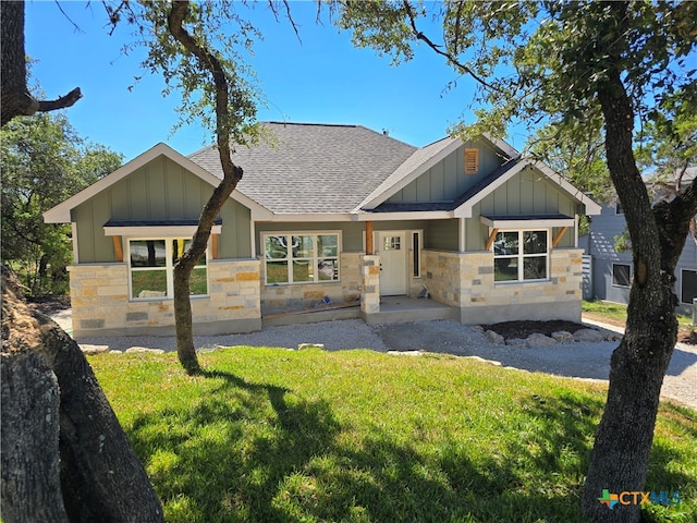 craftsman-style home featuring board and batten siding, a front yard, stone siding, and roof with shingles