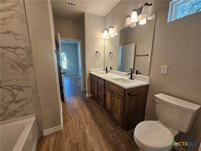 full bath featuring toilet, wood finish floors, a sink, and visible vents