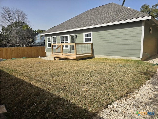 back of property with a wooden deck, fence, a lawn, and roof with shingles