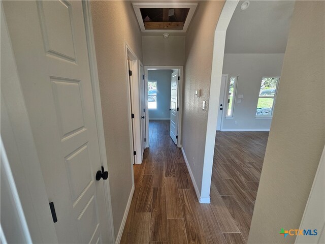 hall featuring baseboards, arched walkways, dark wood-type flooring, and a textured wall