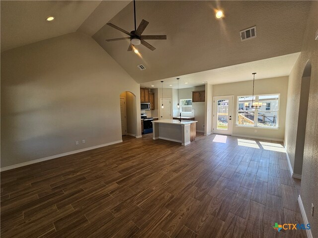 unfurnished living room featuring arched walkways, ceiling fan with notable chandelier, a sink, visible vents, and dark wood finished floors