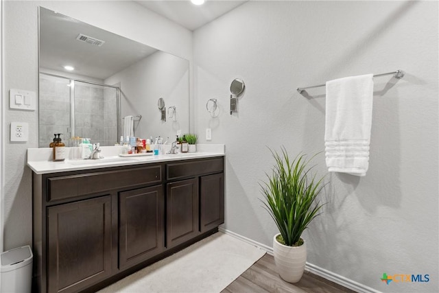 bathroom with double vanity, visible vents, a stall shower, a sink, and wood finished floors