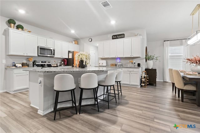 kitchen featuring a kitchen bar, white cabinetry, light stone counters, stainless steel appliances, and a kitchen island with sink