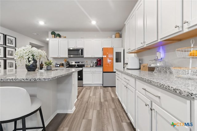 kitchen featuring appliances with stainless steel finishes, a breakfast bar, white cabinetry, light stone counters, and light hardwood / wood-style flooring