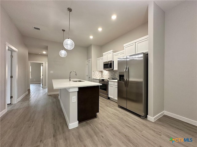 kitchen featuring sink, hanging light fixtures, stainless steel appliances, white cabinets, and a center island with sink