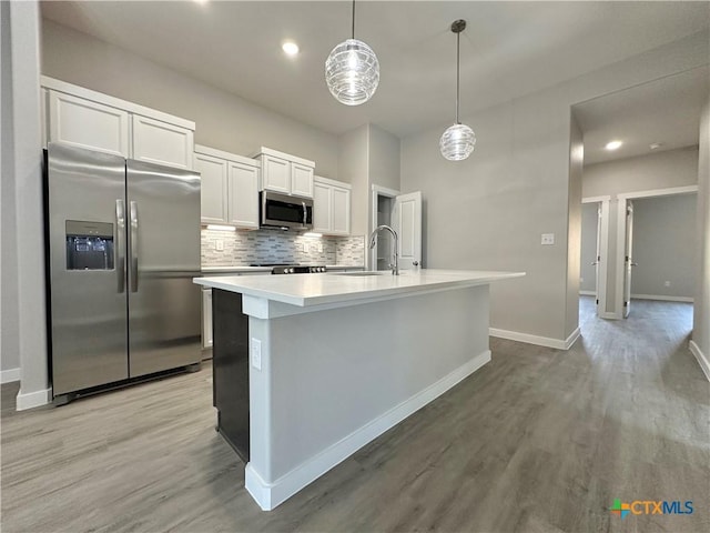 kitchen with white cabinetry, appliances with stainless steel finishes, an island with sink, pendant lighting, and backsplash