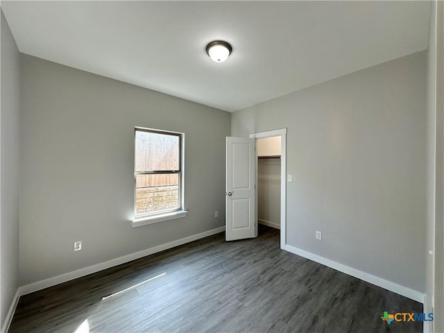 unfurnished bedroom featuring a walk in closet and dark wood-type flooring