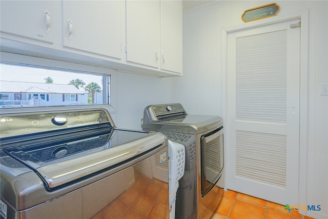 clothes washing area with washing machine and dryer, cabinets, and light tile patterned floors