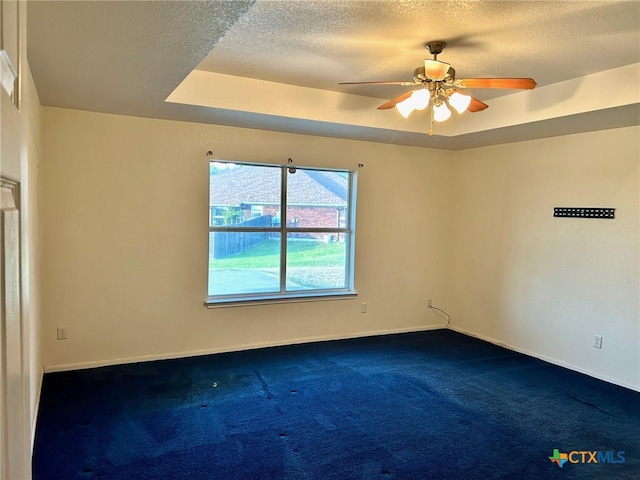 carpeted empty room with a textured ceiling, a tray ceiling, and ceiling fan