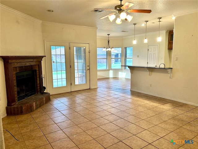 unfurnished living room with light tile patterned floors, ornamental molding, a textured ceiling, a brick fireplace, and ceiling fan with notable chandelier