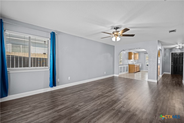 unfurnished living room with a textured ceiling, dark hardwood / wood-style flooring, a wealth of natural light, and ceiling fan