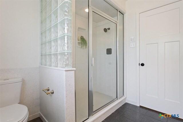 full bath featuring tile walls, toilet, a stall shower, and wainscoting