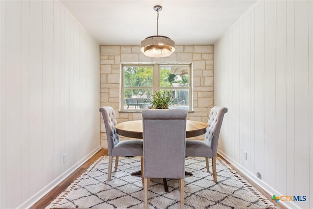 dining space with baseboards, wood walls, and wood finished floors