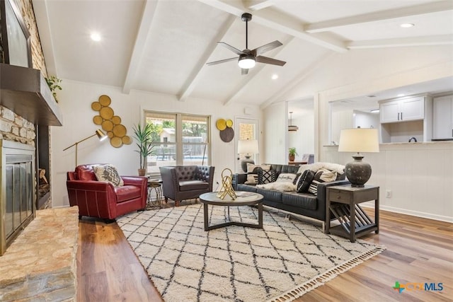 living room featuring lofted ceiling with beams, a ceiling fan, wood finished floors, and a stone fireplace