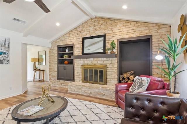 living area with vaulted ceiling with beams, visible vents, a glass covered fireplace, built in shelves, and wood finished floors