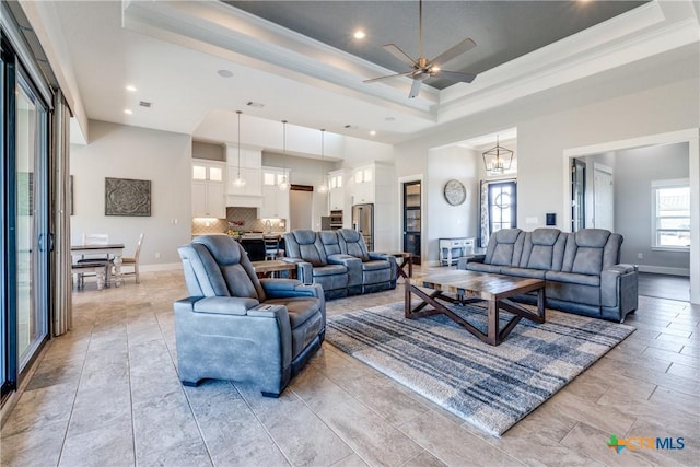 living room featuring ceiling fan with notable chandelier, a tray ceiling, and ornamental molding