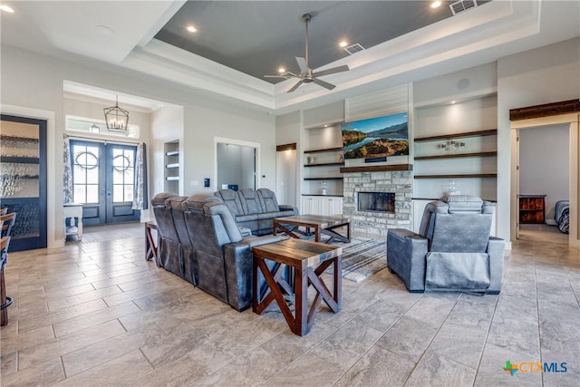 living room featuring ceiling fan with notable chandelier, a raised ceiling, a fireplace, and built in shelves