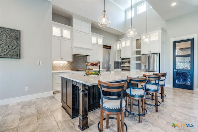 kitchen with a towering ceiling, stainless steel appliances, a spacious island, pendant lighting, and white cabinetry