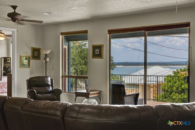 living room with a water view, a textured ceiling, and ceiling fan