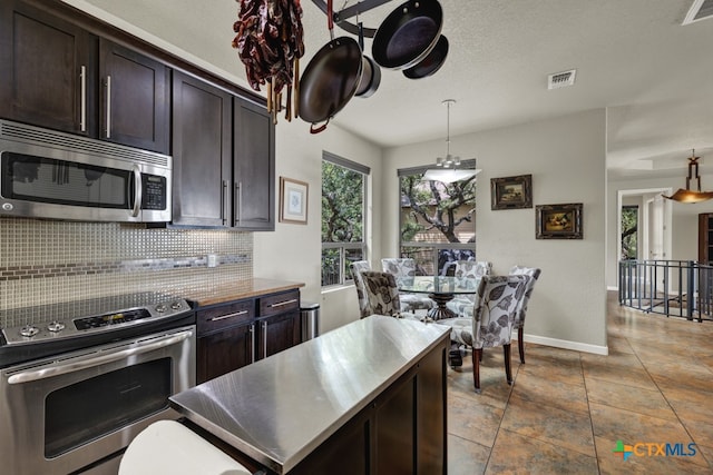 kitchen featuring dark brown cabinetry, stainless steel appliances, pendant lighting, and backsplash