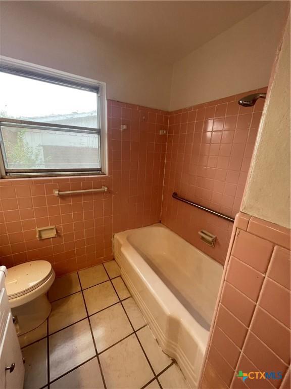bathroom with toilet, shower / tub combination, vanity, tile patterned floors, and tile walls