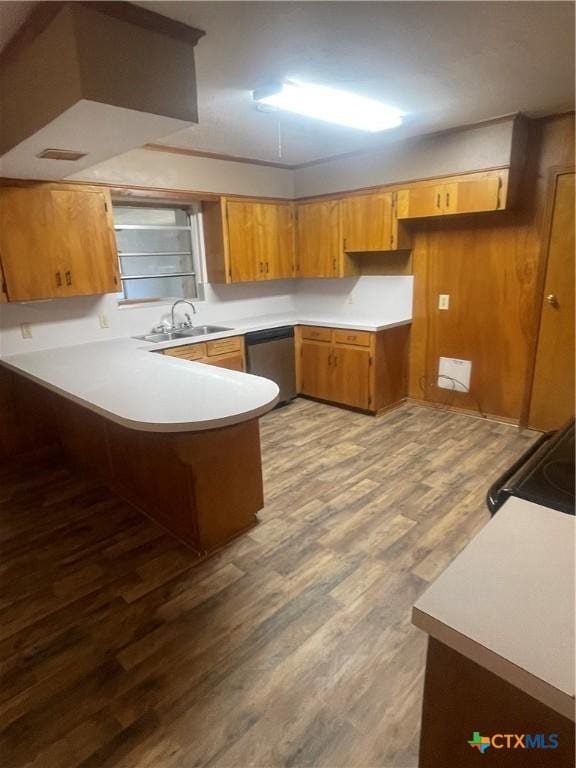 kitchen featuring wood finished floors, brown cabinetry, a peninsula, a sink, and dishwasher