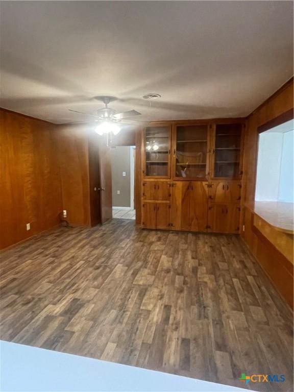 unfurnished living room with a ceiling fan, wooden walls, and wood finished floors