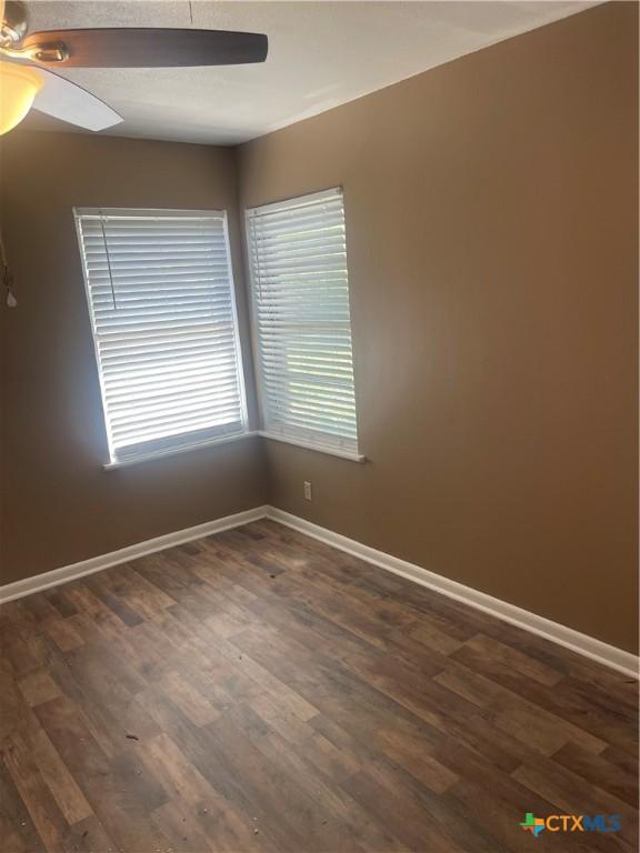 spare room with baseboards, ceiling fan, and dark wood-style flooring