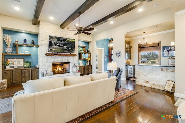 living area featuring baseboards, dark wood-type flooring, a stone fireplace, beam ceiling, and ceiling fan with notable chandelier