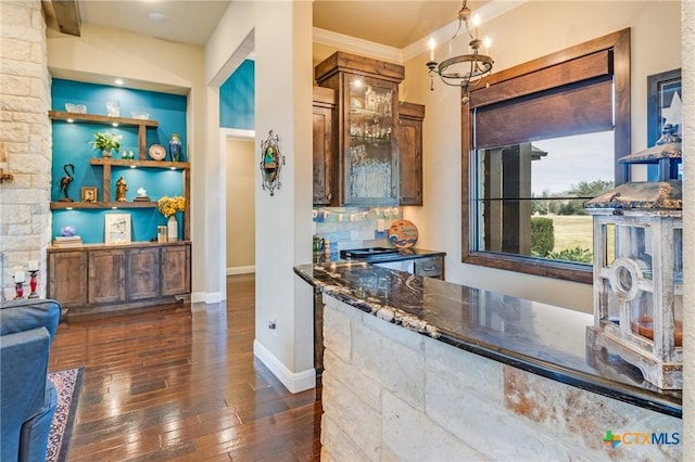 kitchen with built in shelves, an inviting chandelier, crown molding, dark stone countertops, and dark hardwood / wood-style floors