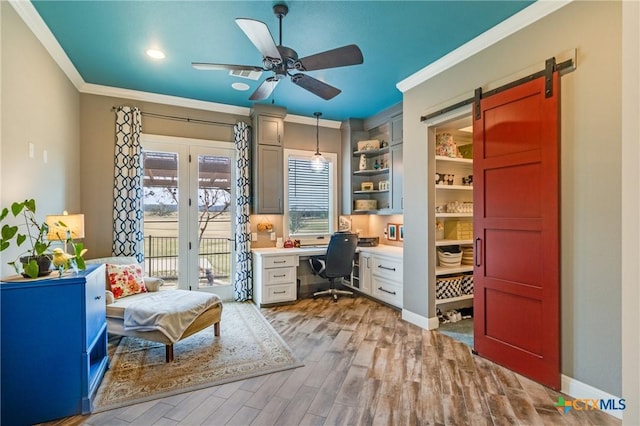 home office with a barn door, ceiling fan, crown molding, and wood finished floors