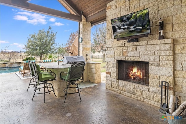 view of patio / terrace featuring a fenced in pool, exterior bar, area for grilling, and an outdoor stone fireplace