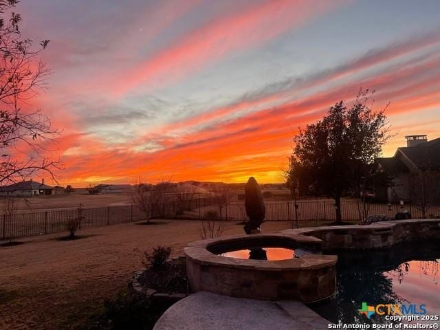 yard at dusk with a fenced backyard and a pool with connected hot tub