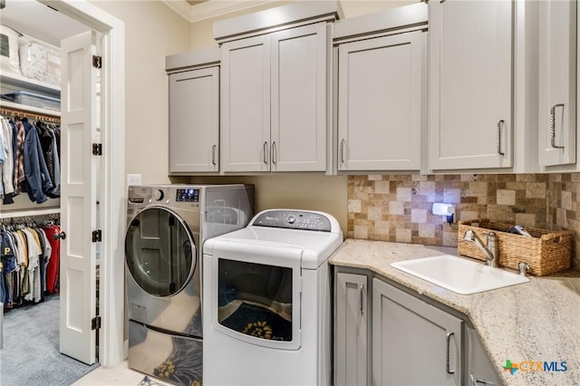 washroom featuring cabinets, ornamental molding, sink, and washing machine and clothes dryer