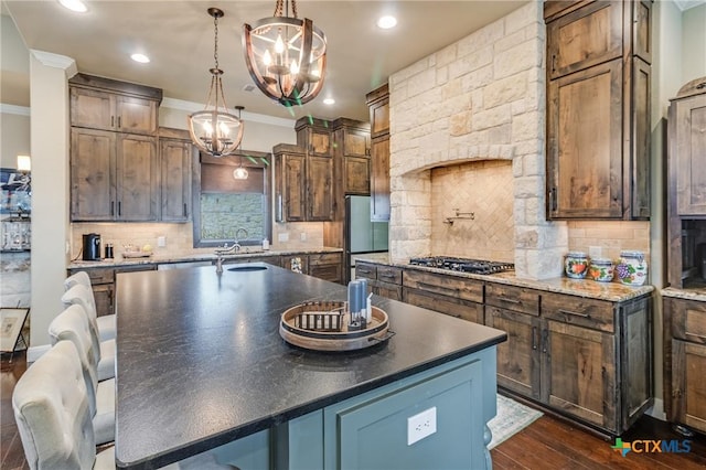 kitchen with stainless steel gas cooktop, ornamental molding, dark wood-style flooring, and a kitchen island with sink