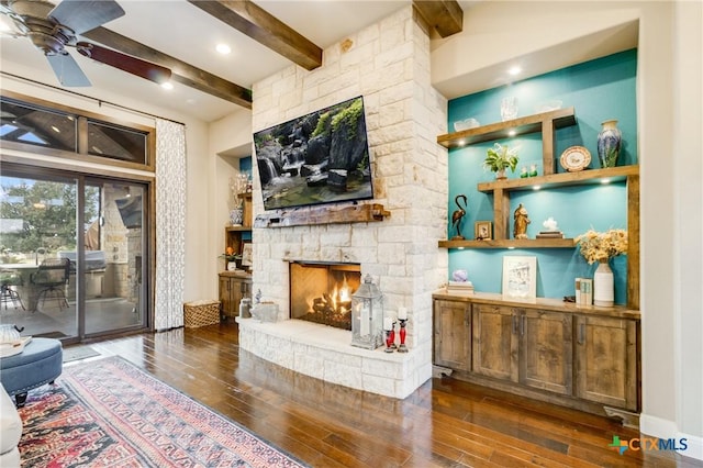 living room featuring ceiling fan, a fireplace, dark hardwood / wood-style flooring, and beam ceiling