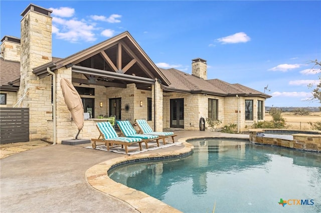 rear view of house with roof with shingles, a chimney, a patio area, ceiling fan, and stone siding