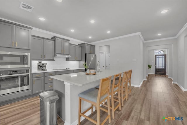 kitchen with light hardwood / wood-style flooring, gray cabinets, a kitchen island with sink, a breakfast bar area, and appliances with stainless steel finishes