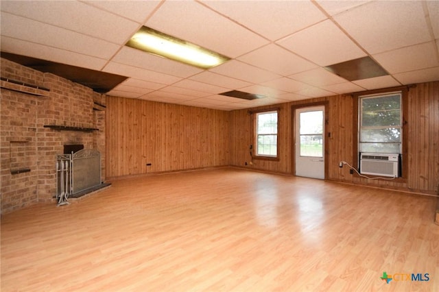 unfurnished living room featuring light wood-type flooring, cooling unit, a drop ceiling, and wood walls